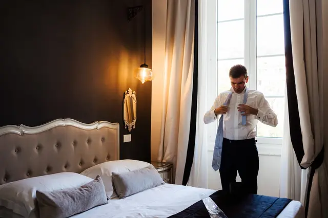 Lo sposo si veste da solo nella camera d’albergo, davanti alla finestra