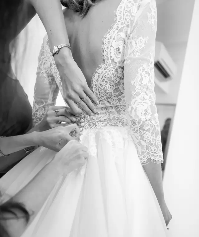 Mani che allacciano i bottoni dell’abito da sposa, sulla schiena