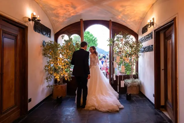 Gli sposi di spalle nell’ingresso a volta del castello, davanti alla porta aperta sulla festa