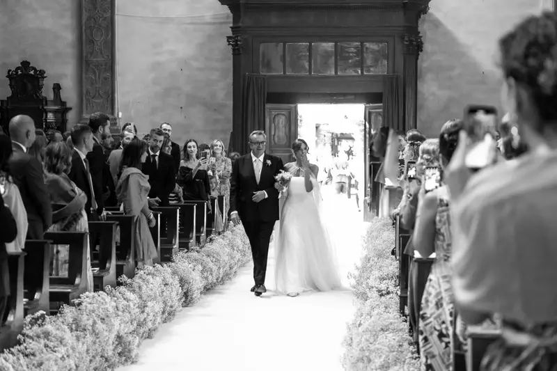 La sposa entra in chiesa a braccetto fra gli invitati, in bianco e nero